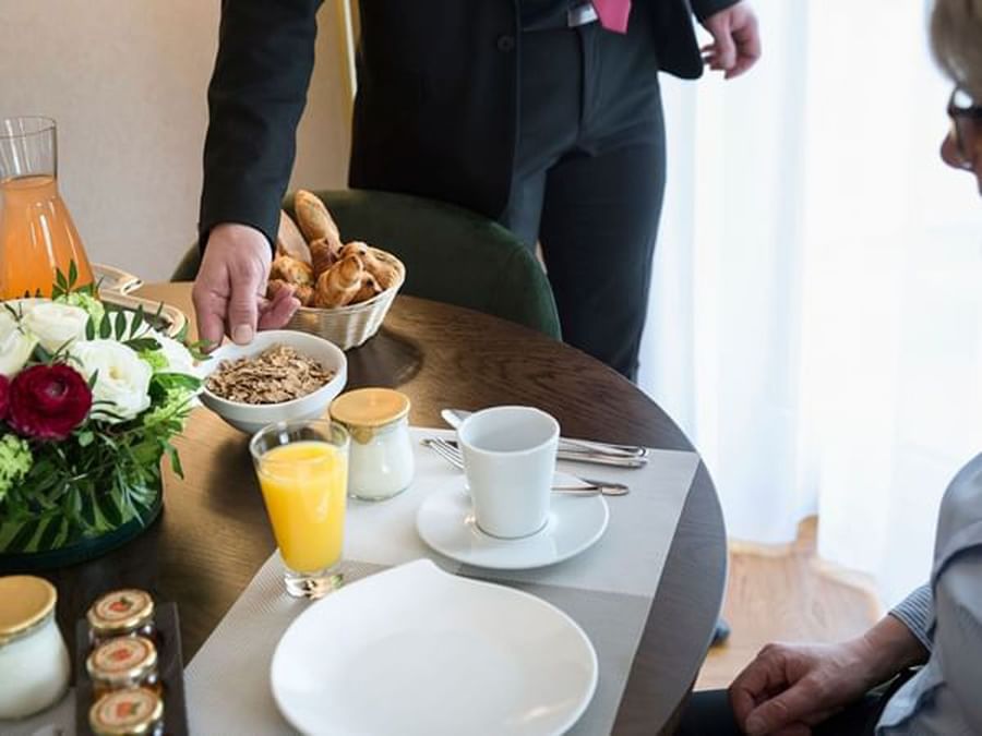 Breakfast setting with a person serving cereal at a table in the Roseraie Room at Warwick Reine Astrid - Lyon