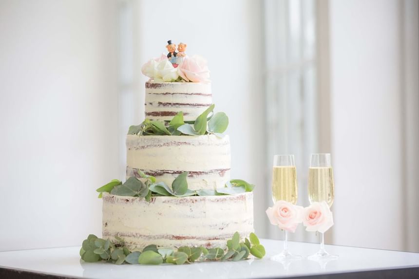 Rustic three-tier wedding cake adorned with flowers and greenery, paired with two champagne flutes at Park Hyatt Saigon