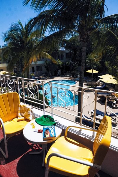 Sunny balcony with yellow chairs and a book overlooking the pool and tropical palm trees at Tradewinds Apartment Hotel