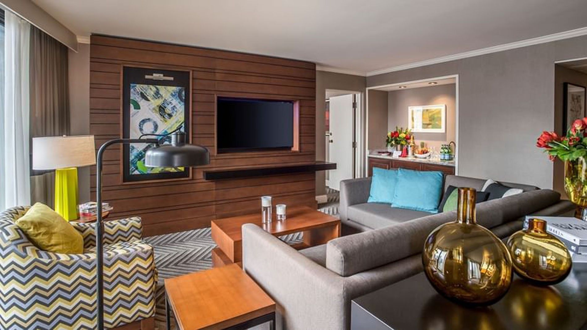 A spacious living room with a sofa, armchairs, coffee table, and TV on a wooden wall.