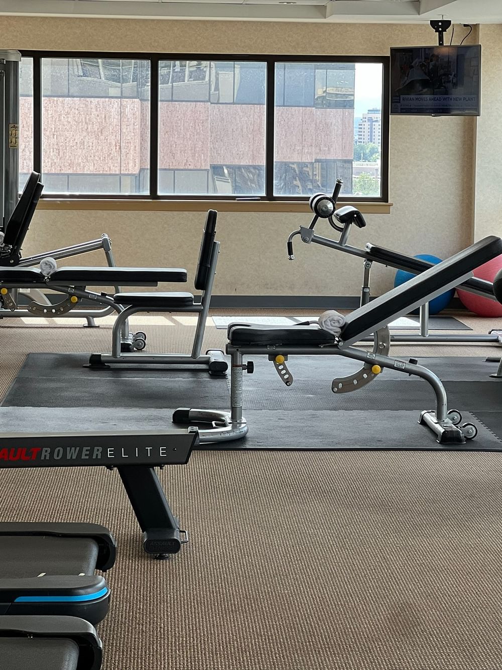 Gym weight benches by a rowing machine under a flat screen near windows at Warwick Denver