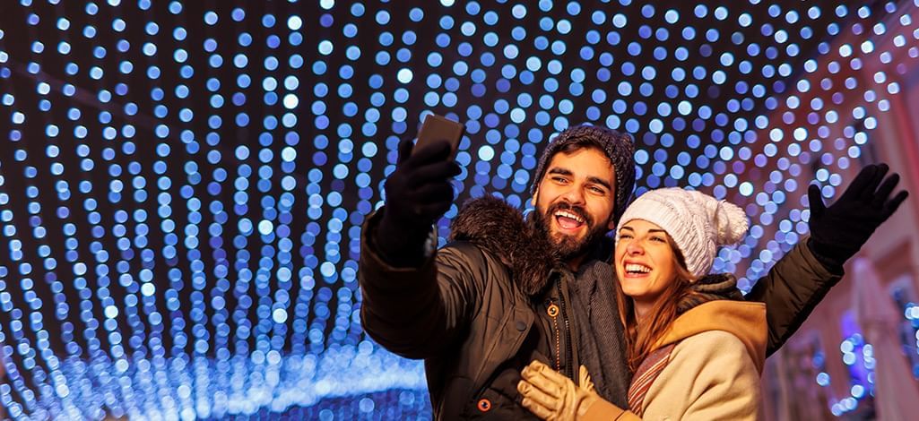 couple taking selfies under christmas lights