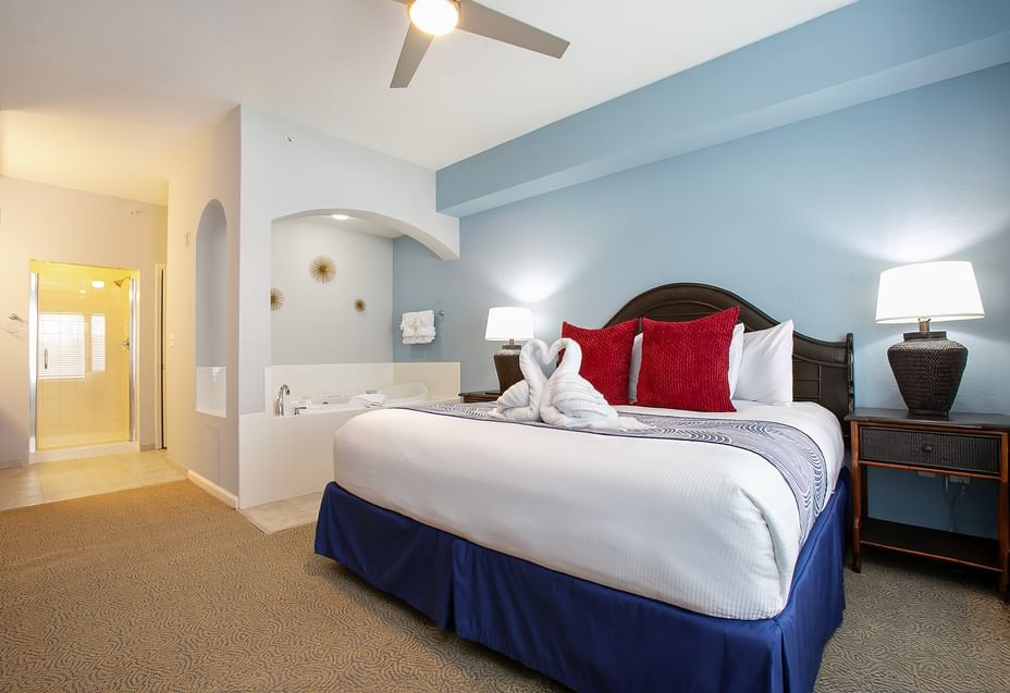 A wide-angle view of a hotel room with a large bed, nightstands, and a ceiling fan.