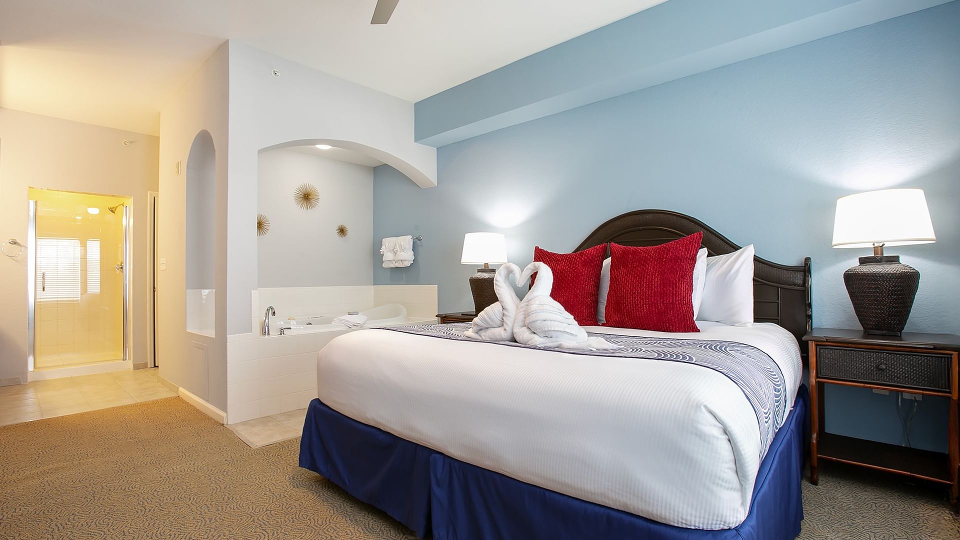 A hotel room with a large bed, two nightstands with lamps, and an archway leading to a bathroom.