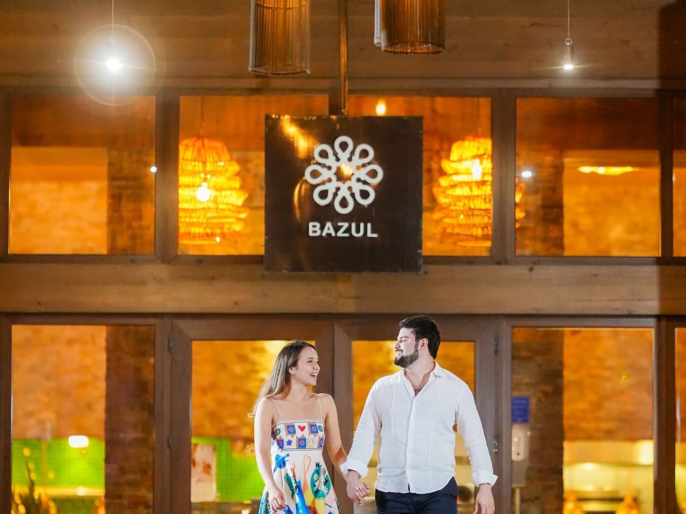 Couple holding hands in front of Bazul Restaurant with warm lighting at Indura Beach & Golf Resort