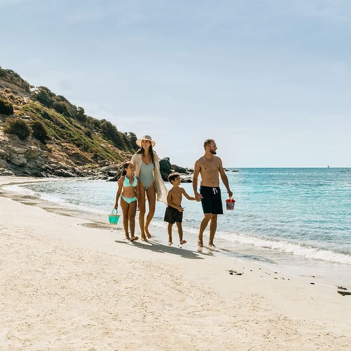 Family walking on a beach by the sea on sunny day near Falkensteiner Resort Capo Boi