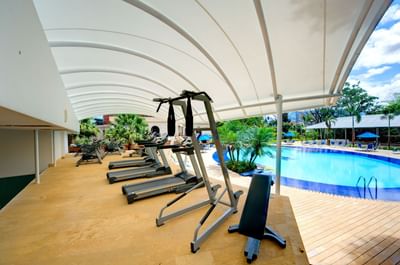 Cintas de correr y equipos de gimnasia en el gimnasio junto a la piscina en el Hotel Dann Carlton Medellín