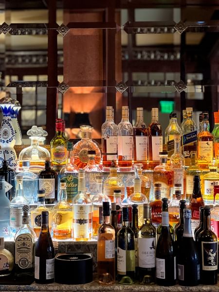 Premium liquor bottles on glass shelves by a mirrored wall in The Library at Warwick Melrose Dallas