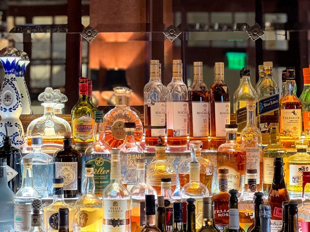 Premium liquor bottles on glass shelves by a mirrored wall in The Library at Warwick Melrose Dallas