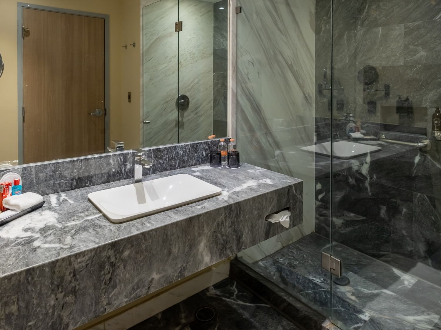 Baño moderno con mármol gris, lavabo blanco, ducha de vidrio y amenidades en Camino Real Fashion Drive Monterrey.