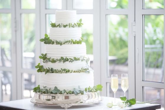 Tiered wedding cake adorned with eucalyptus leaves, by two champagne flutes on a silver platter at Park Hyatt Saigon