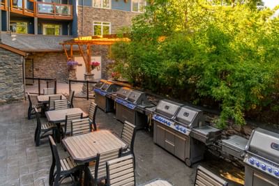 Sunlit outdoor grilling area with multiple stainless steel barbecues and wooden table at Blackstone Mountain Lodge