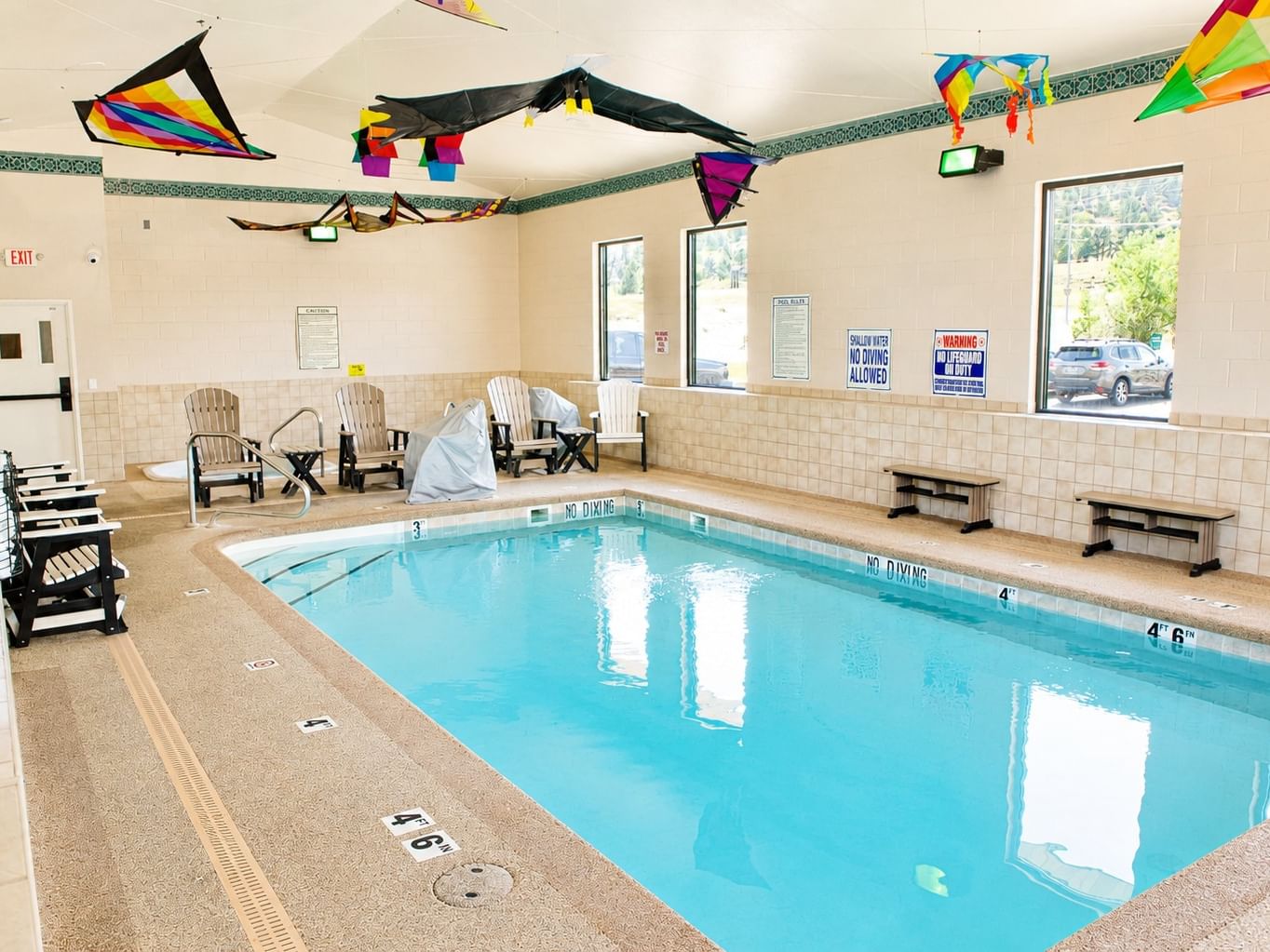 Indoor heated pool with colorful kite decorations, lounge chairs, and beige tile walls at Booking - Boothill Inn
