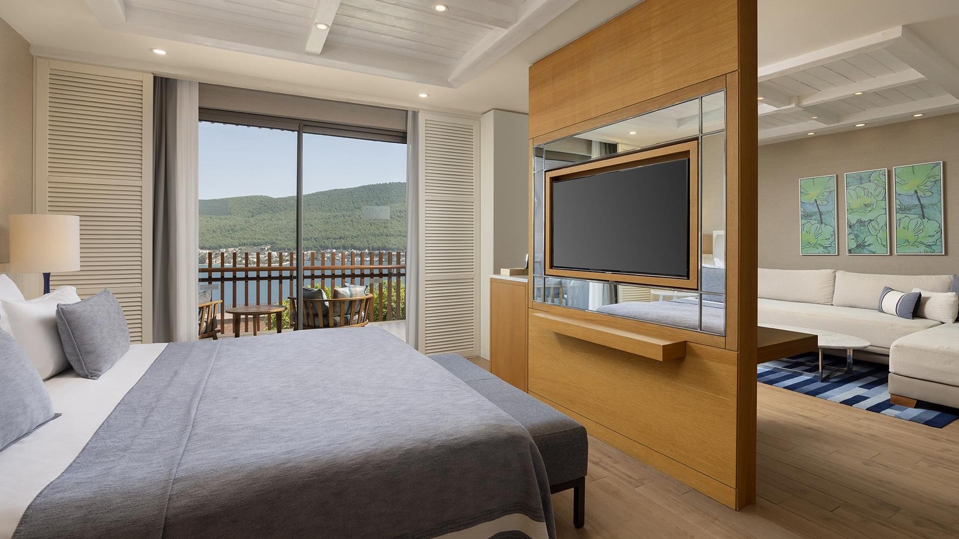 Deluxe Sea View Room's bedroom with a large bed, balcony, TV, and couch with a sea view at Titanic Luxury Collection Bodrum.