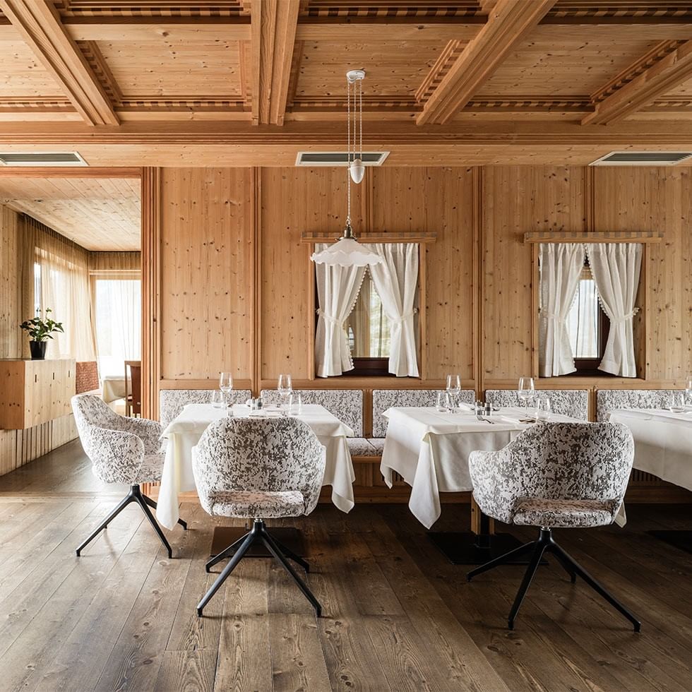Wooden interior of a dining area with three tables, each with four chairs, and a hanging lamp.