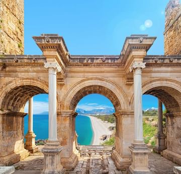 Hadrian Gate with three arched openings overlooking a serene blue sea under a clear sky.