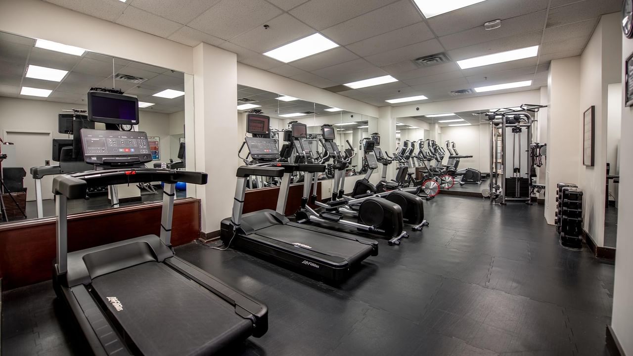 Hotel gym with multiple treadmills, weight machines, and mirrors.
