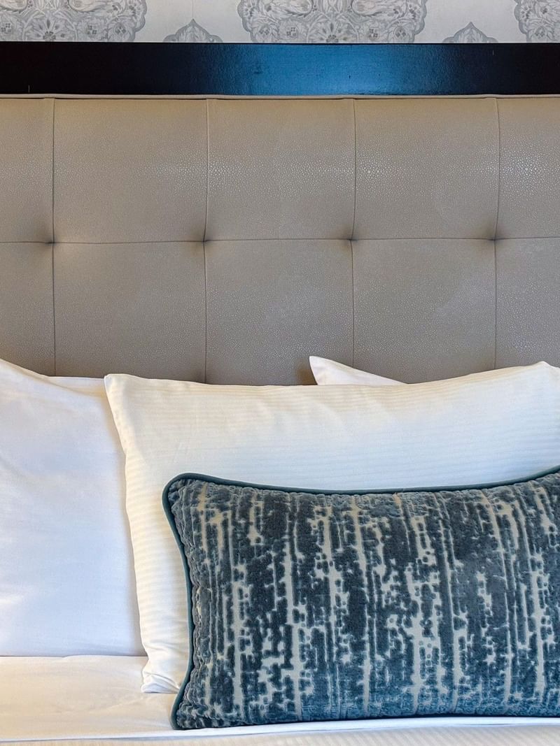 Close-up of a tufted beige headboard with white pillows and blue textured cushions in Premier Suite at Warwick New York