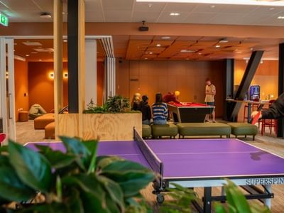Modern recreation lounge with ping pong table, pool table, and guests enjoying games in warm-toned interior at Tupuārangi