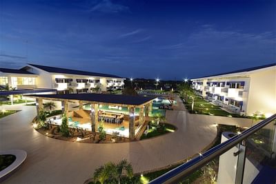 An aerial night view of Hotel Mykonos with lit hotel buildings and a central outdoor bar and pool