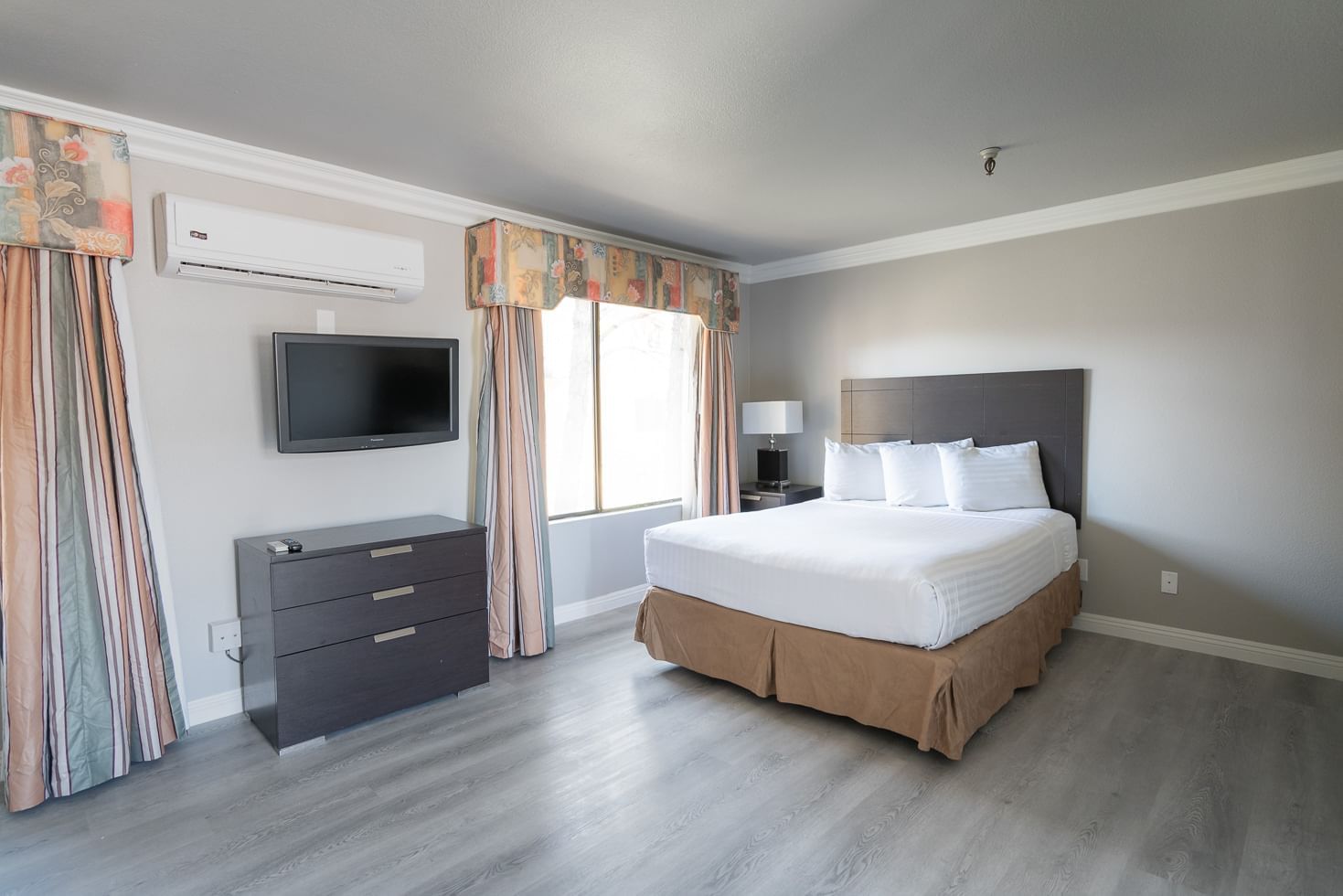 A hotel room with a queen bed, TV, and window
