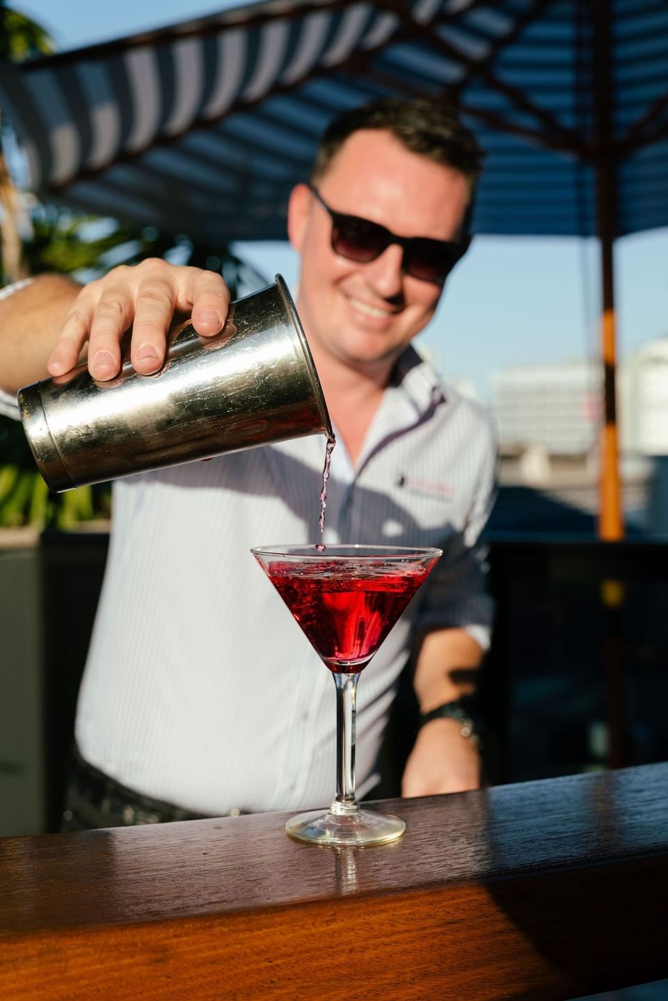 Bartender pouring a red cocktail into a martini glass in an outdoor bar at H on Mitchell