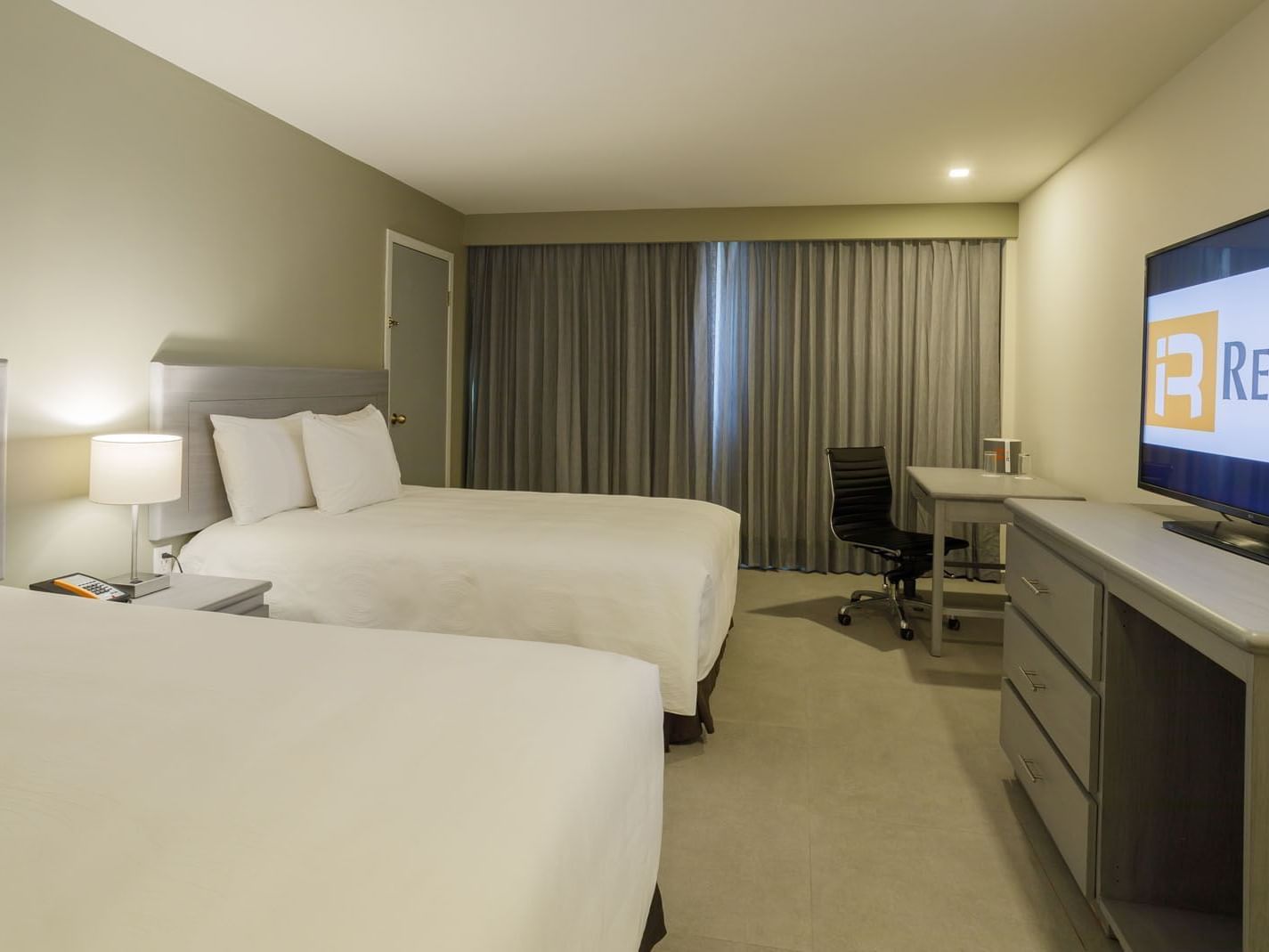 2 Double Deluxe room featuring two beds, a work desk, and the hotel brand displayed on TV at Real Inn Mexicali