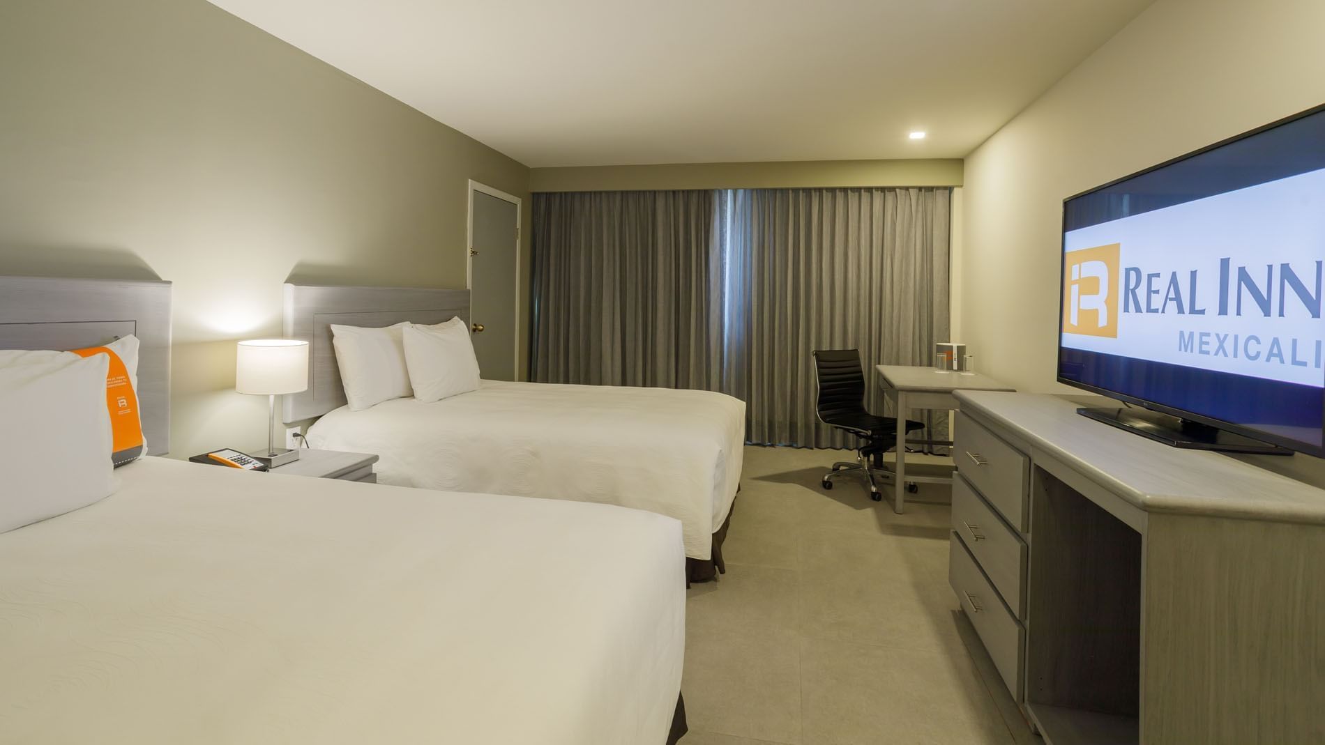 2 Double Deluxe room featuring two beds, a work desk, and the hotel brand displayed on TV at Real Inn Mexicali