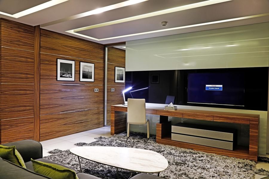 Wooden desk by a TV under a recessed ceiling near a marble coffee table in Executive Suite at Warwick Stone 55 - Beirut