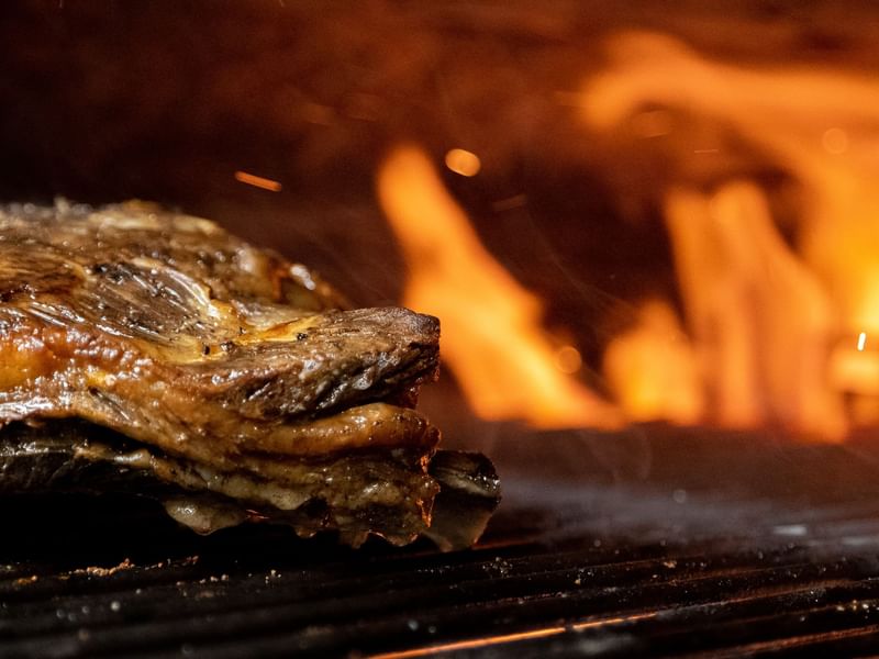 Grilled steak on a black grill with a fire flame background at Hotel Hacienda del Mar los Cabos