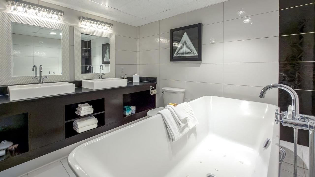 Modern bathroom with white soaking tub, dual vessel sinks, dark vanity, and contemporary lighting at Coast Calgary University Area Hotel by APA
