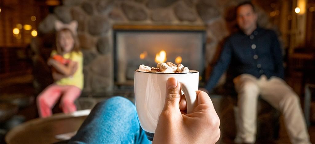 A family sits in a Canmore hotel lounge by the fire, drinking hot chocolate.