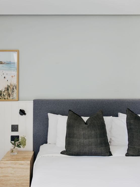 Coastal Two Bedroom Suite at Elysium Manly with dark cushions placed on a white bed by a wooden side table under a framed