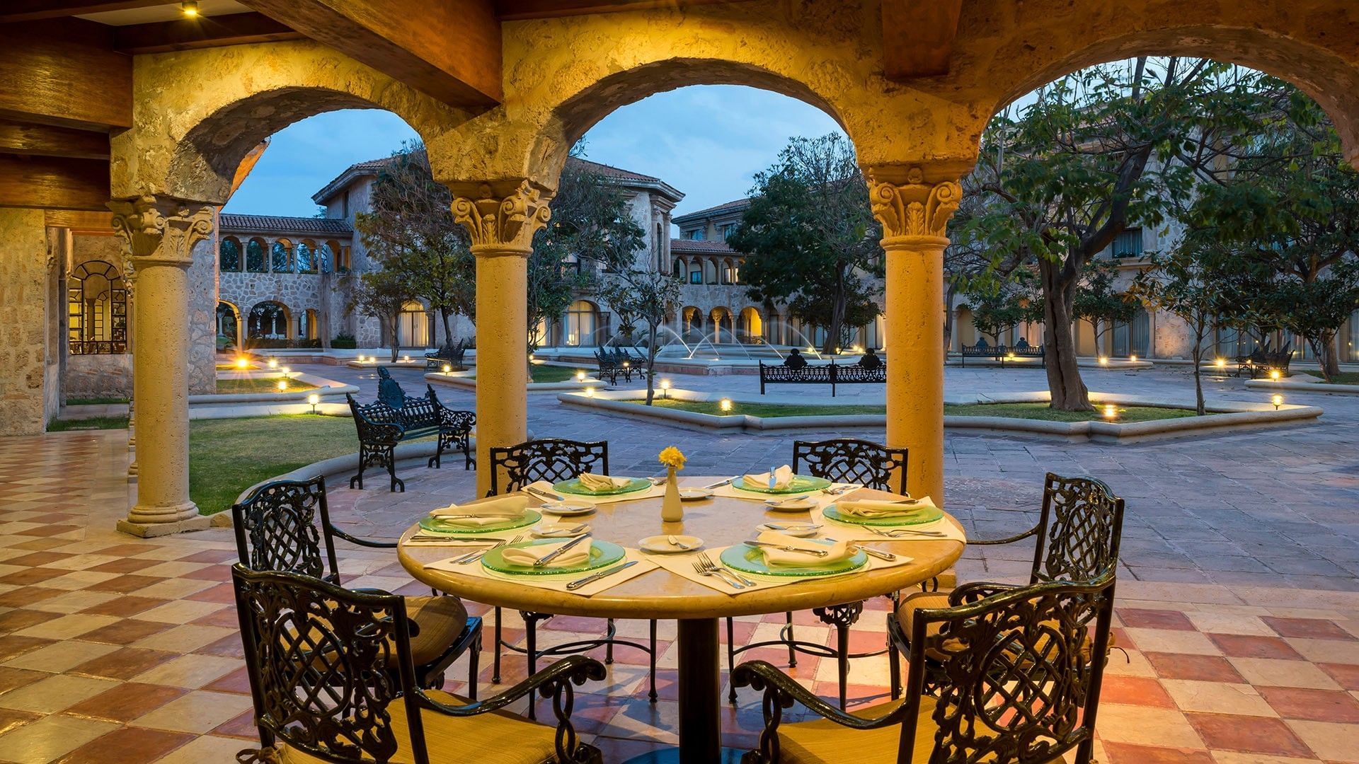 Mesa redonda con manteles amarillos bajo arcos coloniales con vista al patio en Tierra Mía, Quinta Real Aguascalientes