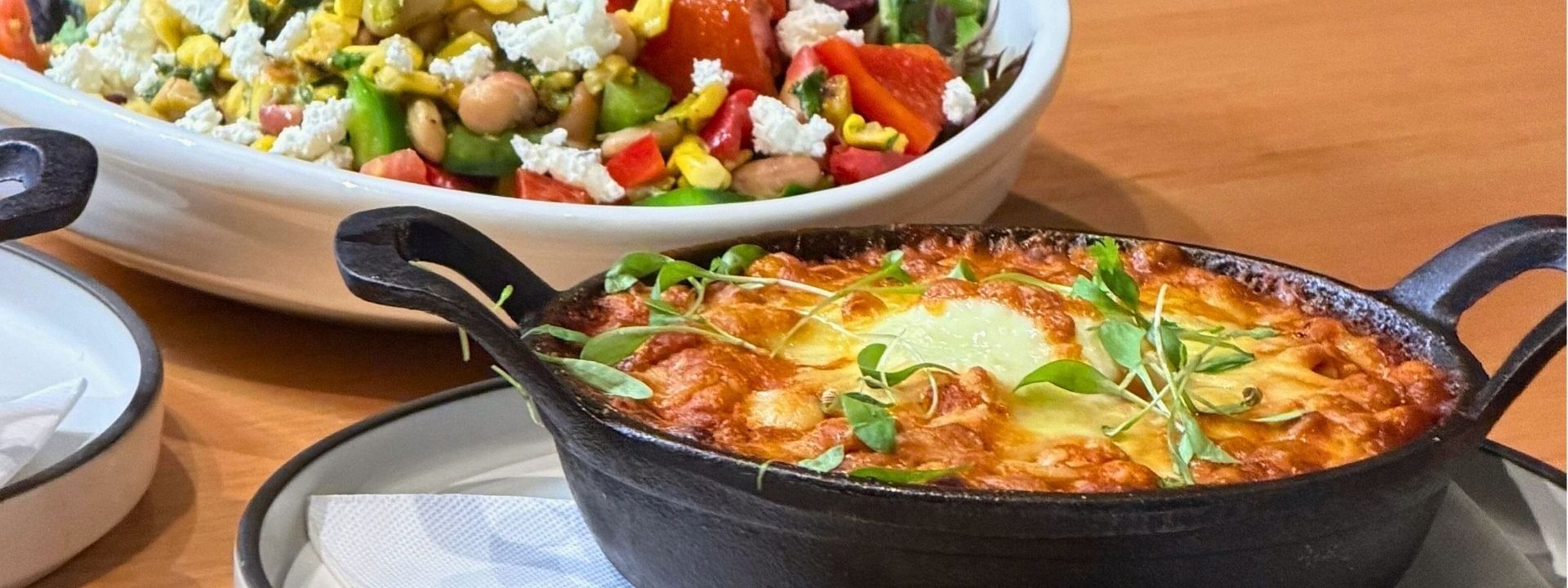 Bowl of salad and pot of gratin chickpeas dish with bread on a table in Pulse Flavours offer.