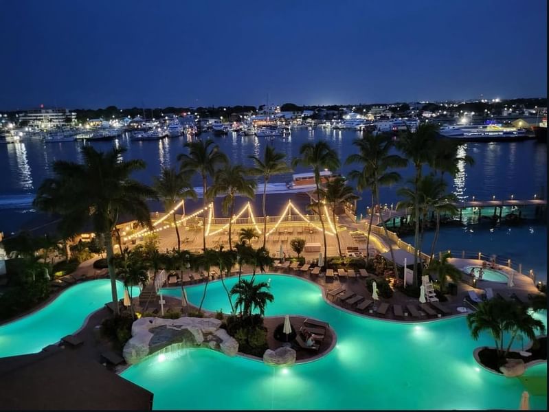 Illuminated lagoon-style pool with palm trees and marina view at dusk at Warwick Paradise Island Nassau Bahamas