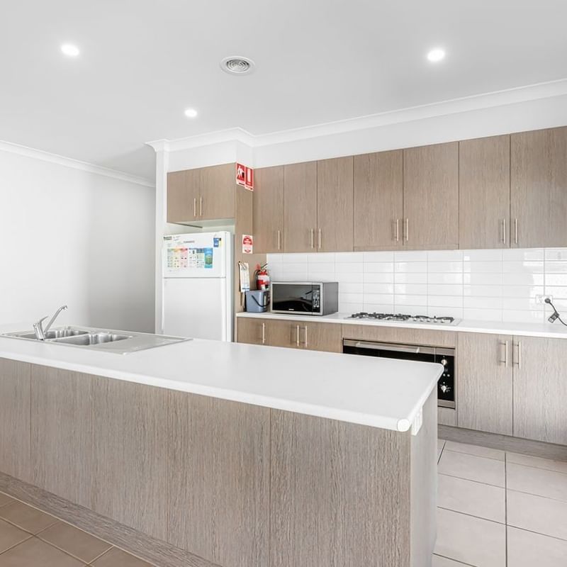 A bright and modern kitchen with white and brown cabinetry, appliances, and a large counter at La Trobe University Regional Housing – Mildura.