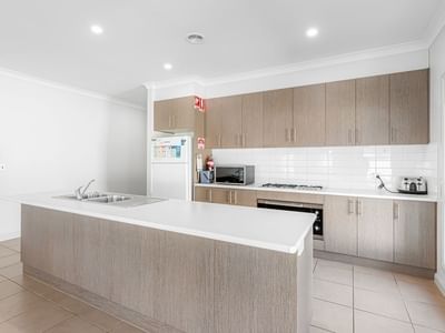 A bright and modern kitchen with white and brown cabinetry, appliances, and a large counter at La Trobe University Regional Housing – Mildura.