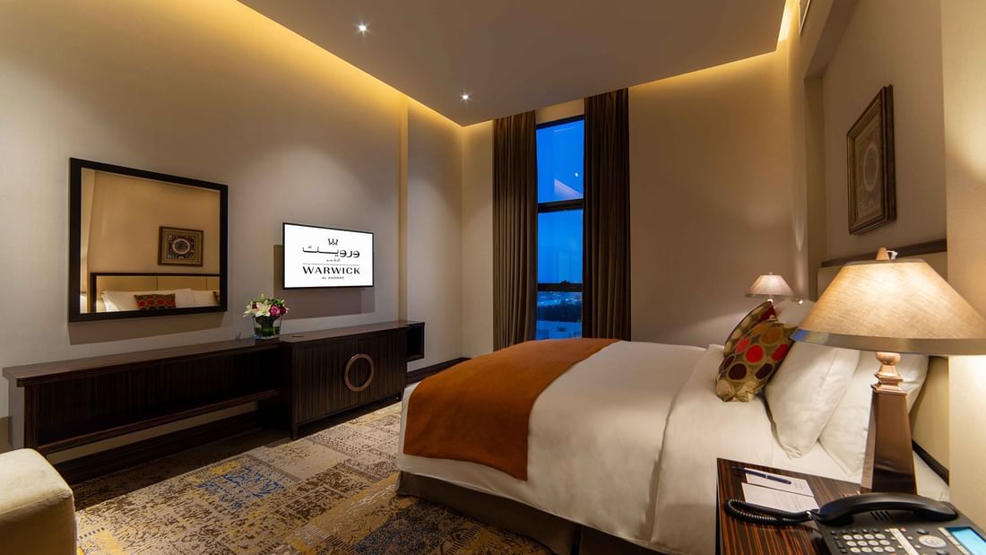 TV & wall mirror facing king bed in Business Suite at Warwick Al Khobar