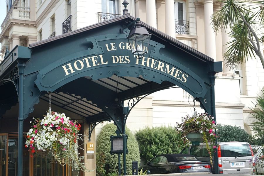 The ornate dark green canopy marks the entrance of Le Grand Hôtel des Thermes with flower deco
