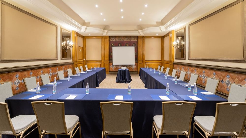 Salon Torre Ejecutiva U-shape meeting setup with blue linens and a large projector screen at Quinta Real Monterrey