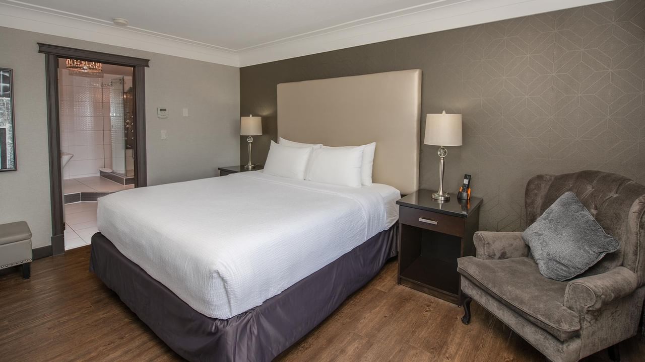 Guest room with king bed, armchair, nightstand, and view into bathroom at Coast Calgary University Area Hotel by APA