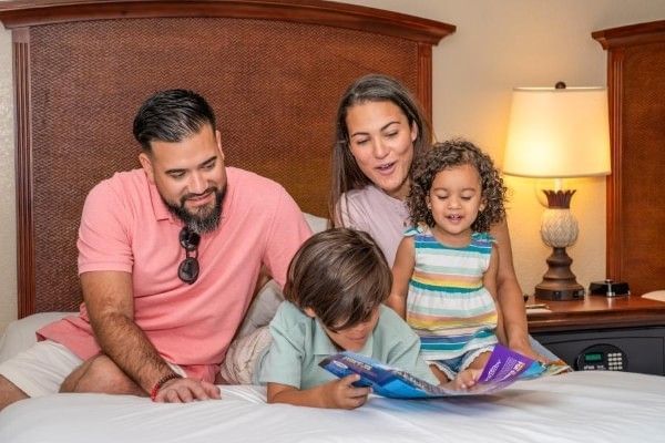 A mom, dad, and two kids sit on a bed at Rosen Inn, looking through a brochure together.