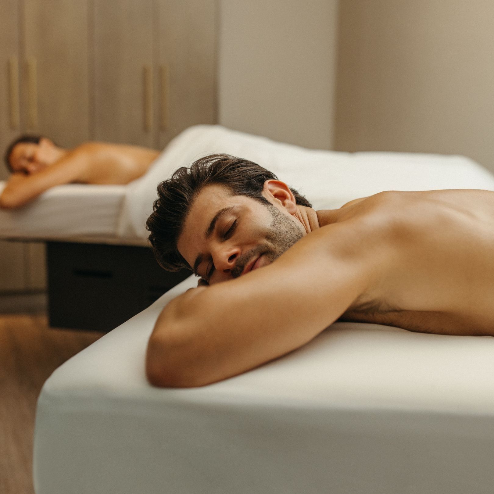 Couple relaxing face-down on massage tables side by side in a dim treatment room at Hotel X Toronto