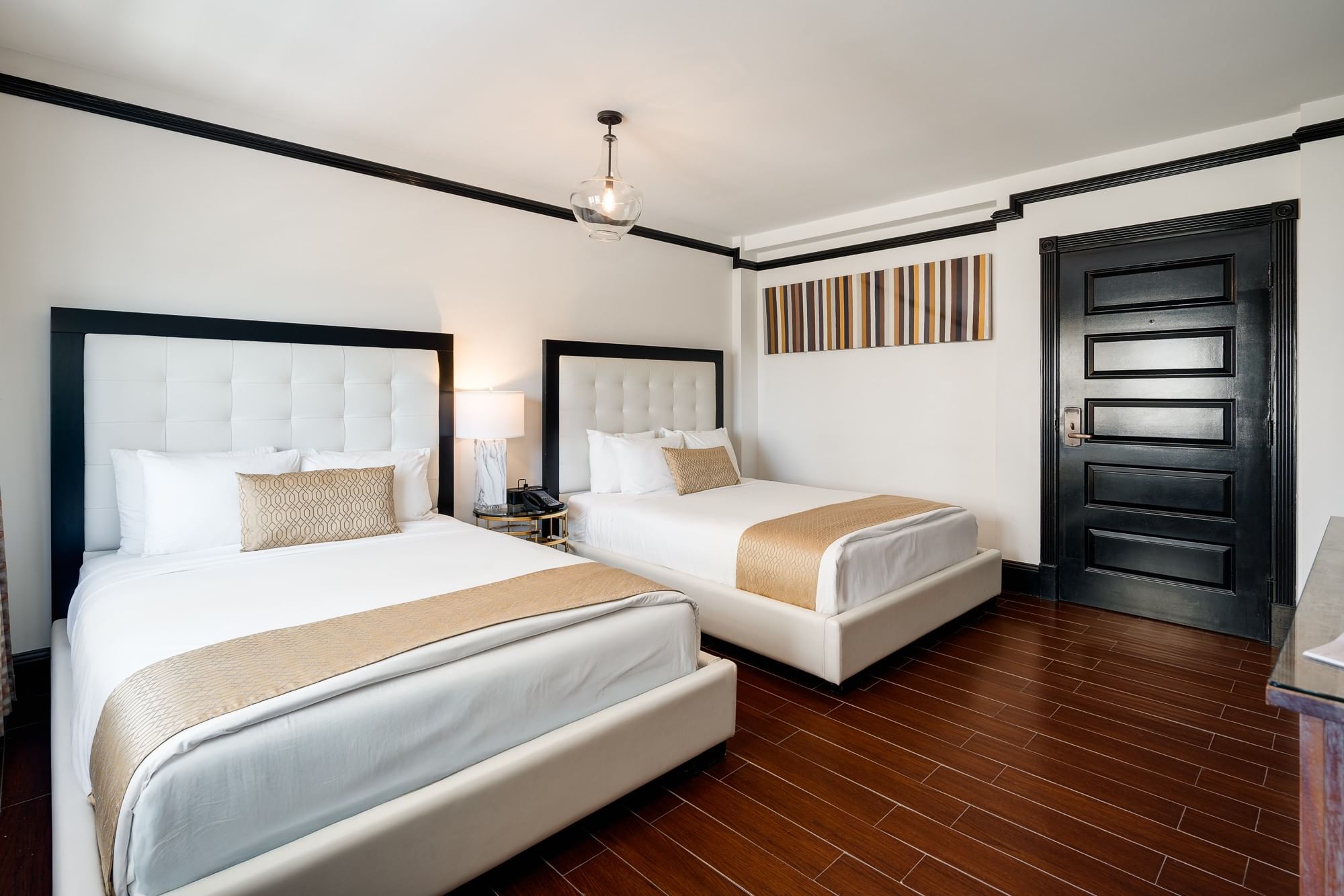 A hotel room with two queen beds, white bedding, and dark wood floors