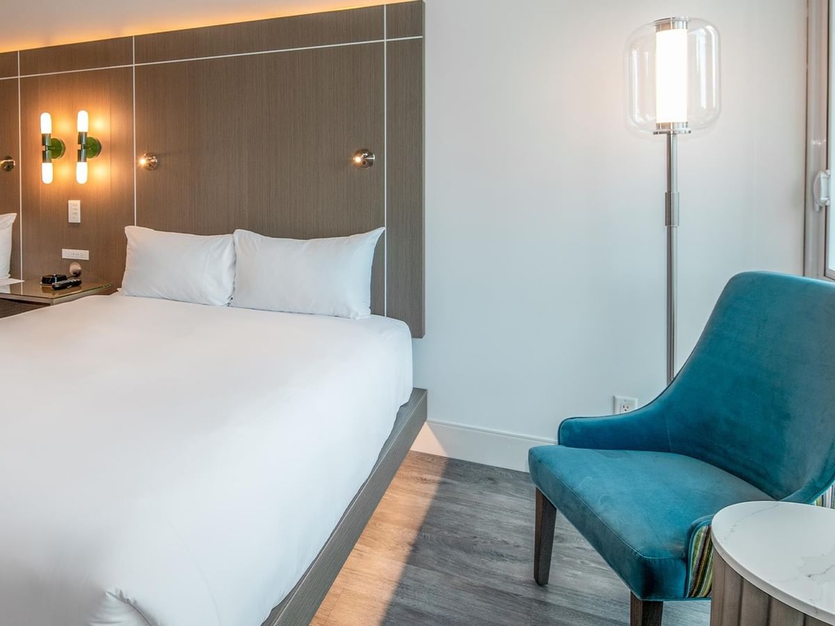 Two queen beds with white bedding, blue chair, and modern decor.