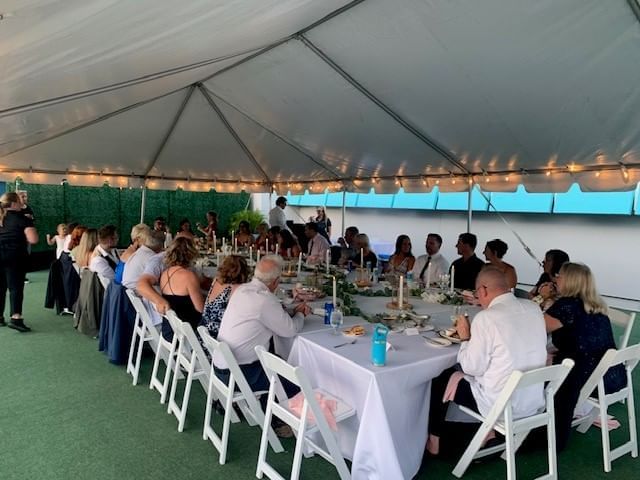 A large group of people sitting at a long table under a tent.