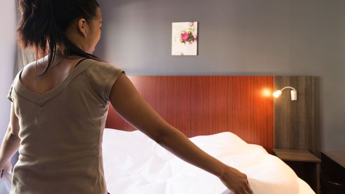 A lady arranging a bed in a room at Le Mas de Grille