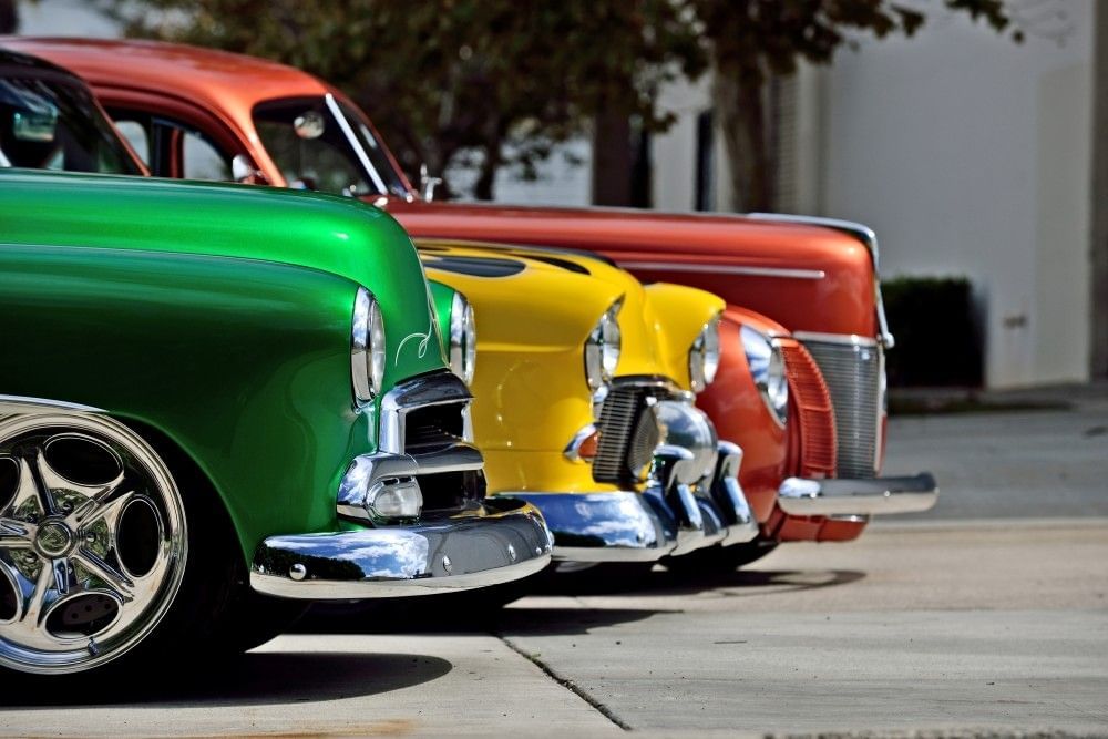 The fronts of green, yellow, and red vintage cars. 