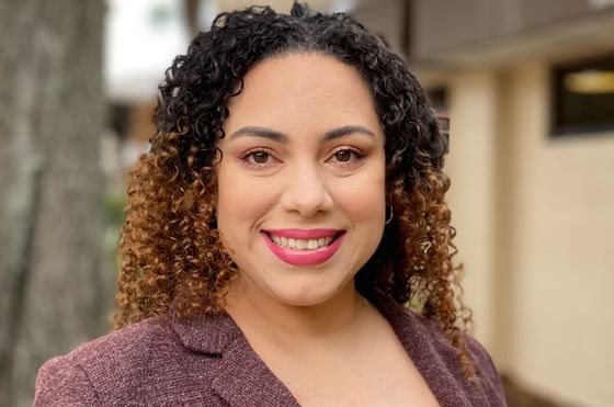 Vanessa Ramirez with dark curly hair, wearing a brown blazer outdoors at Rosen Inn at Pointe Orlando